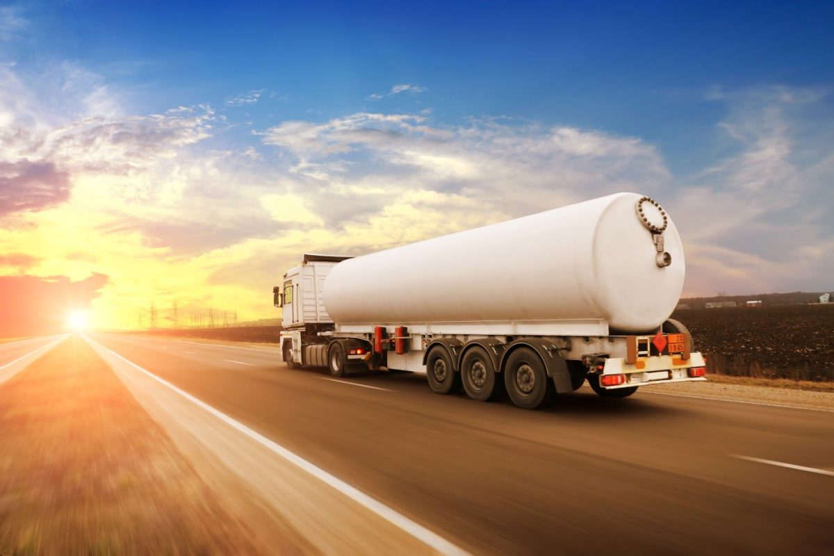 White oil and gas tanker truck driving on a road at sunset