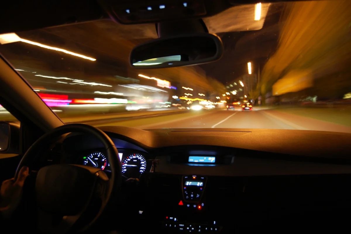 View from inside a car at night, looking through the windshield at blurred city lights while driving.